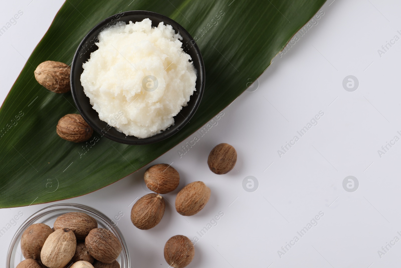 Photo of Natural shea butter in bowl, nuts and green leaf on white background, top view. Space for text