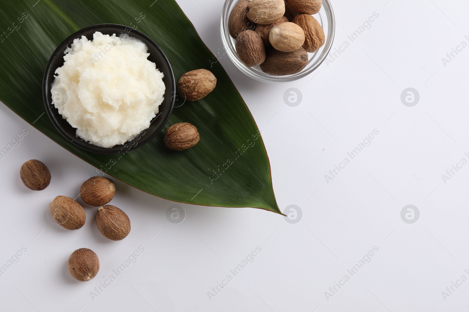 Photo of Natural shea butter in bowl, nuts and green leaf on white background, top view. Space for text