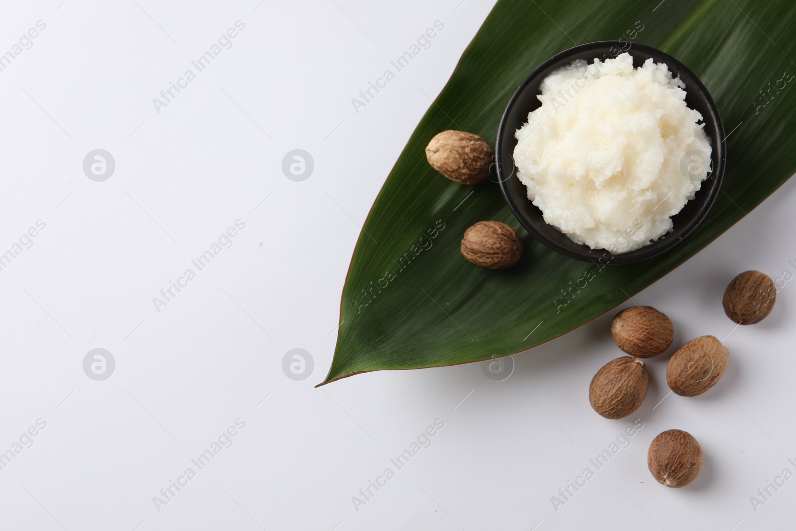 Photo of Natural shea butter in bowl, nuts and green leaf on white background, top view. Space for text