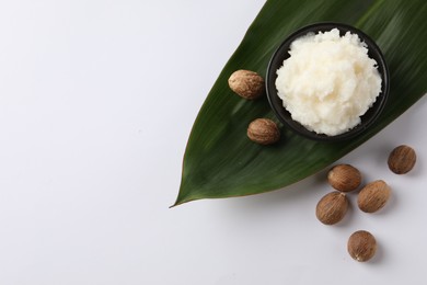 Natural shea butter in bowl, nuts and green leaf on white background, top view. Space for text