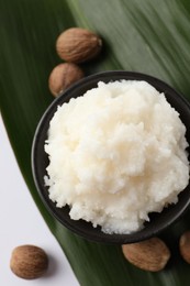 Photo of Natural shea butter in bowl, nuts and green leaf on white background, top view