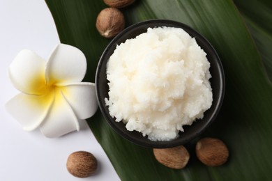 Natural shea butter in bowl, nuts, plumeria flower and green leaf on white background, top view