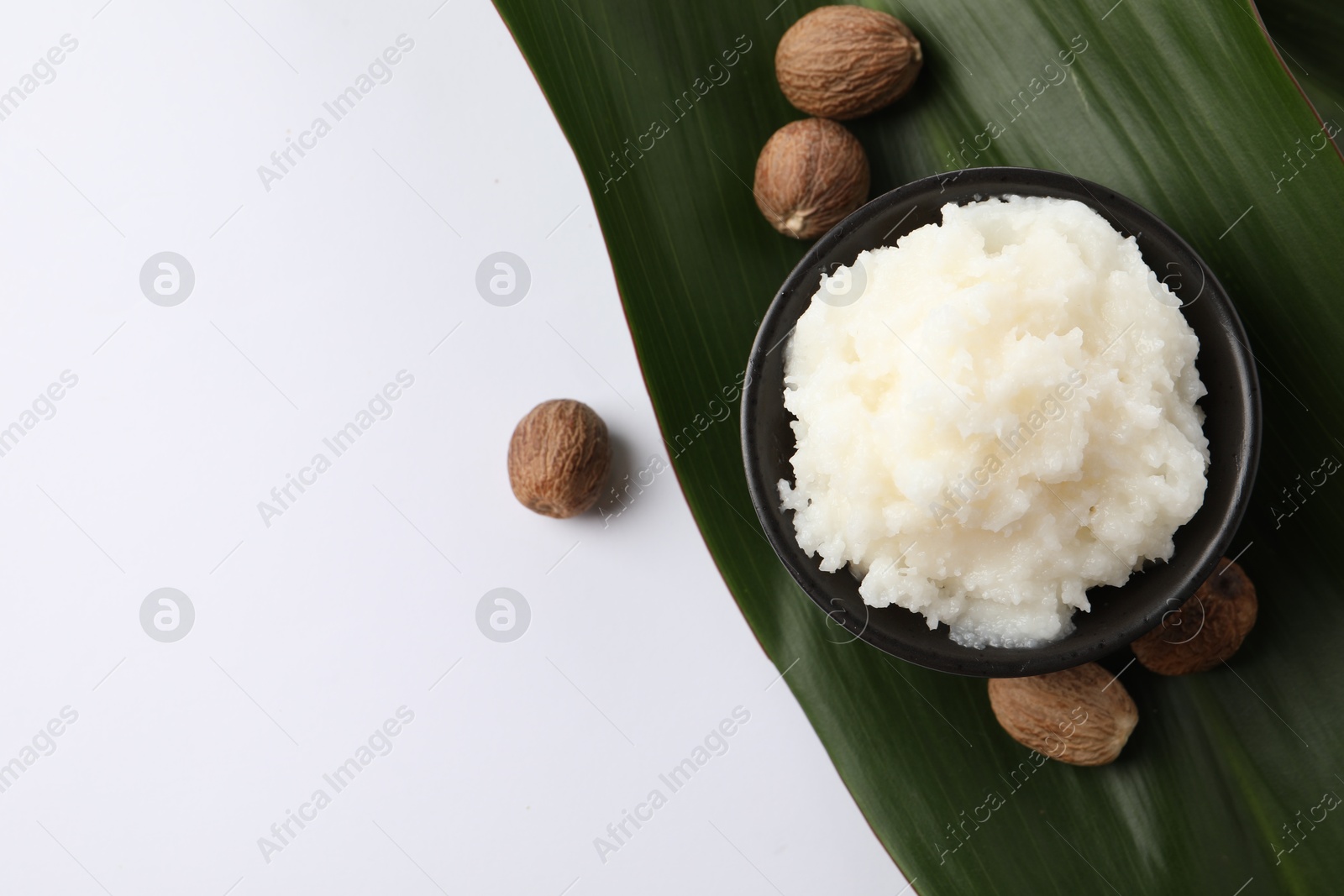 Photo of Natural shea butter in bowl, nuts and green leaf on white background, top view. Space for text