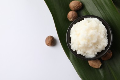 Natural shea butter in bowl, nuts and green leaf on white background, top view. Space for text