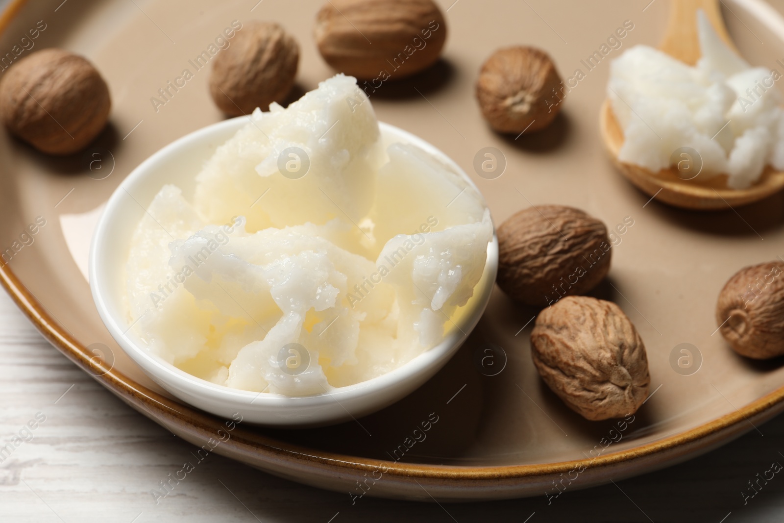 Photo of Natural shea butter in bowl and nuts on wooden table, closeup