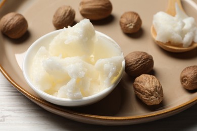 Natural shea butter in bowl and nuts on wooden table, closeup