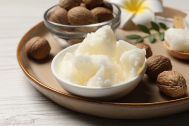 Photo of Natural shea butter in bowl, nuts, plumeria flower and green twig on wooden table, closeup