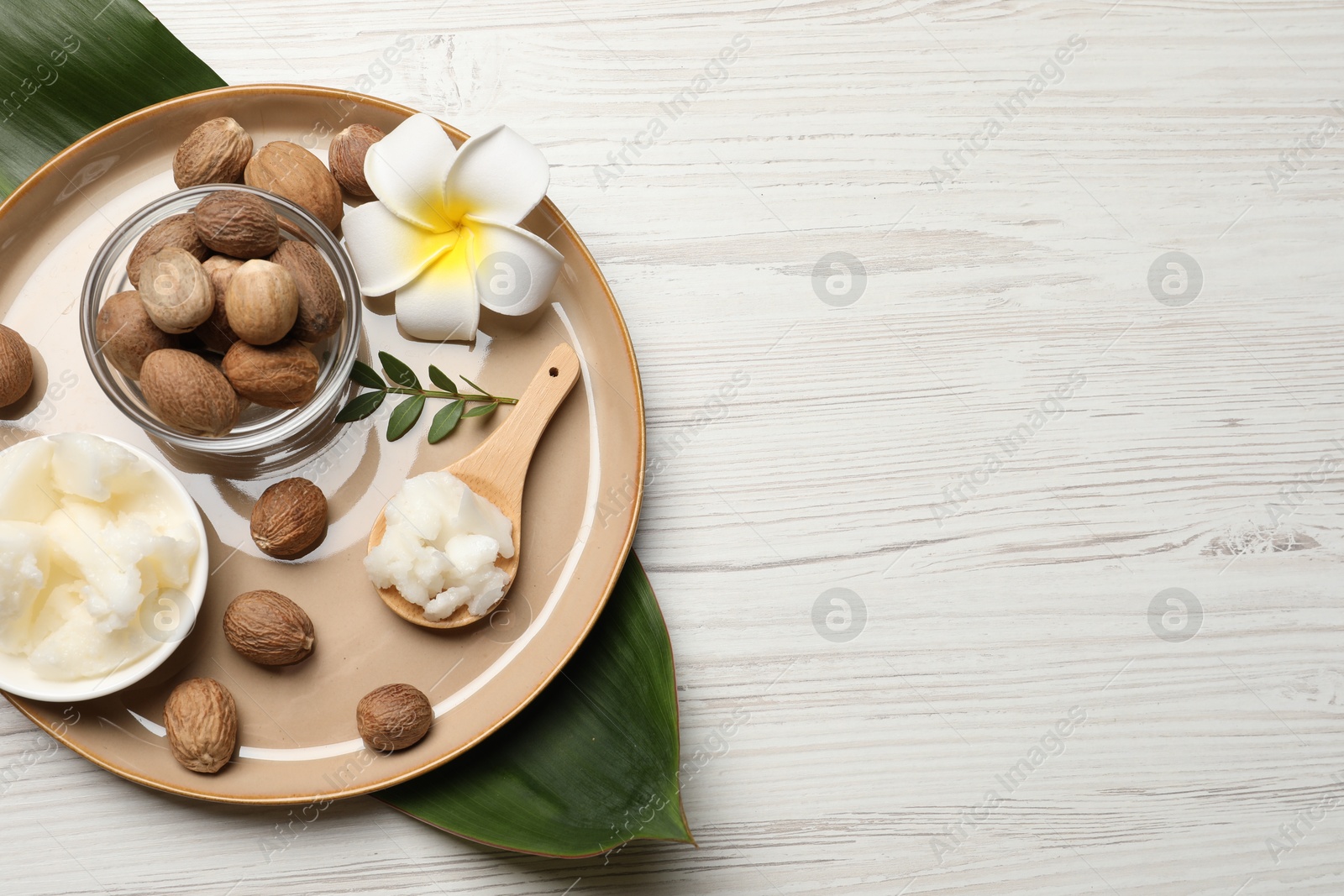 Photo of Natural shea butter in bowl, nuts, plumeria flower and green leaves on wooden table, top view. Space for text