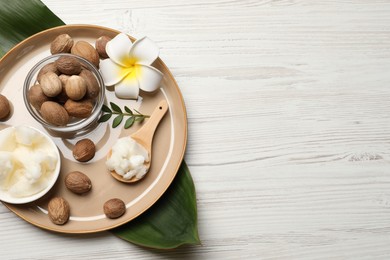 Natural shea butter in bowl, nuts, plumeria flower and green leaves on wooden table, top view. Space for text