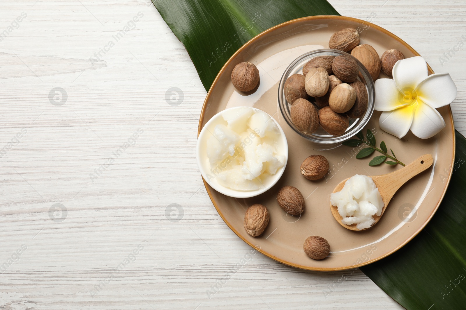 Photo of Natural shea butter in bowl, nuts, plumeria flower and green leaves on wooden table, top view. Space for text