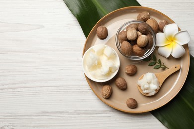 Photo of Natural shea butter in bowl, nuts, plumeria flower and green leaves on wooden table, top view. Space for text