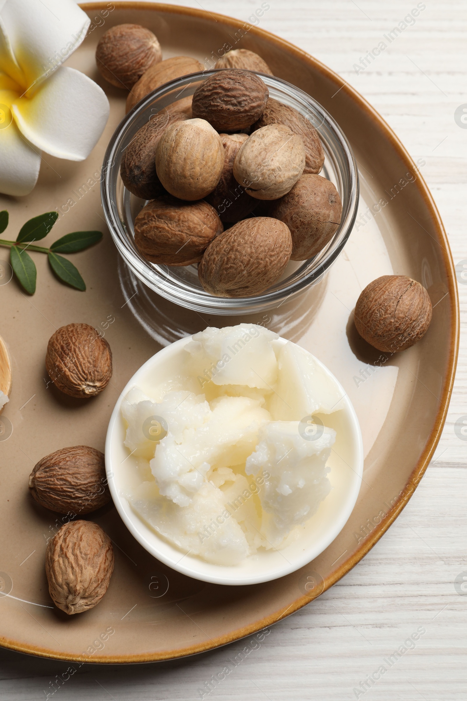 Photo of Natural shea butter in bowl, nuts, plumeria flower and green twig on wooden table, top view