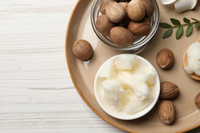 Photo of Natural shea butter in bowl, nuts and green twig on wooden table, top view. Space for text