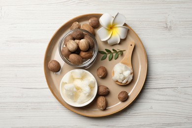 Photo of Natural shea butter in bowl, nuts, plumeria flower and green twig on wooden table, top view