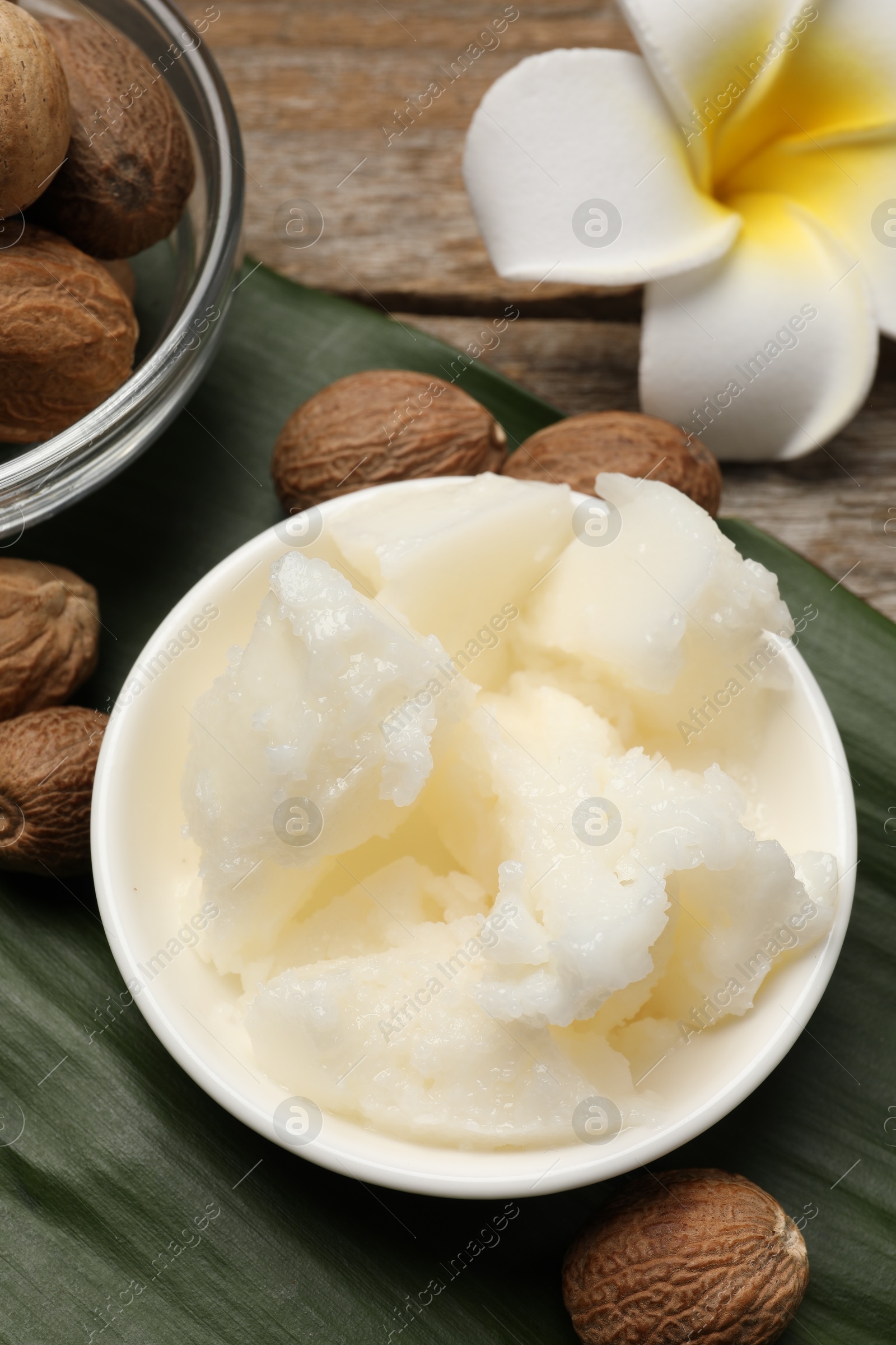 Photo of Natural shea butter in bowl, nuts, plumeria flower and green leaf on wooden table