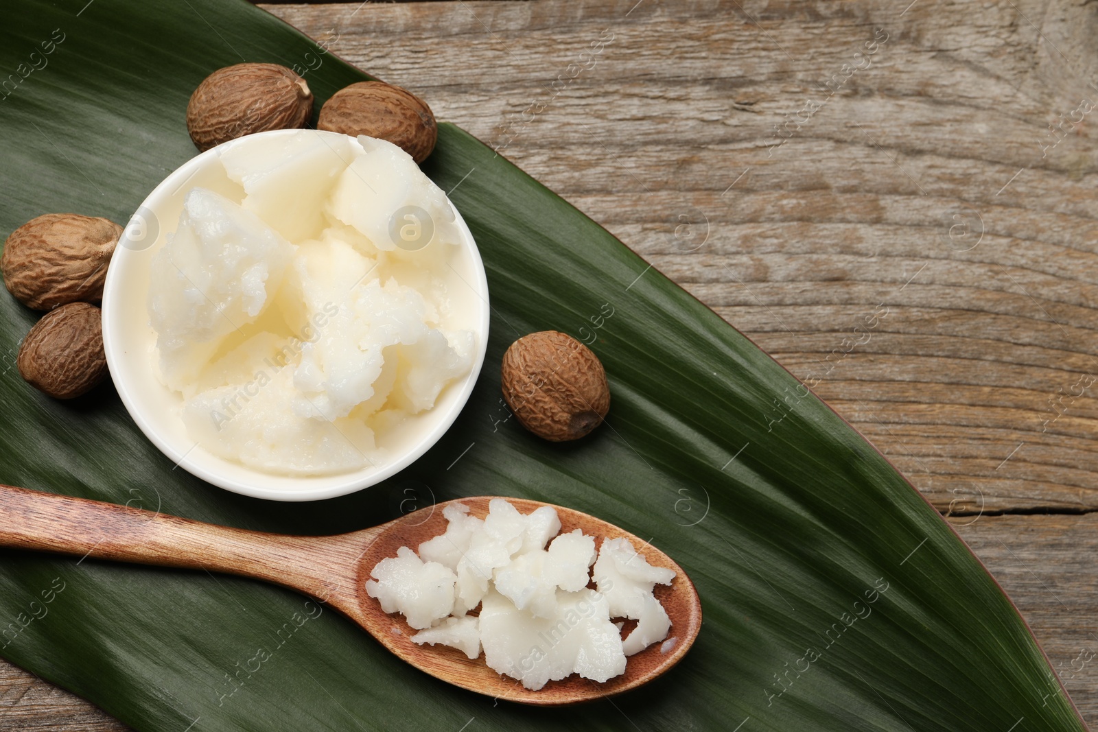 Photo of Natural shea butter in bowl, spoon, nuts and green leaf on wooden table, top view