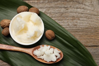 Natural shea butter in bowl, spoon, nuts and green leaf on wooden table, top view