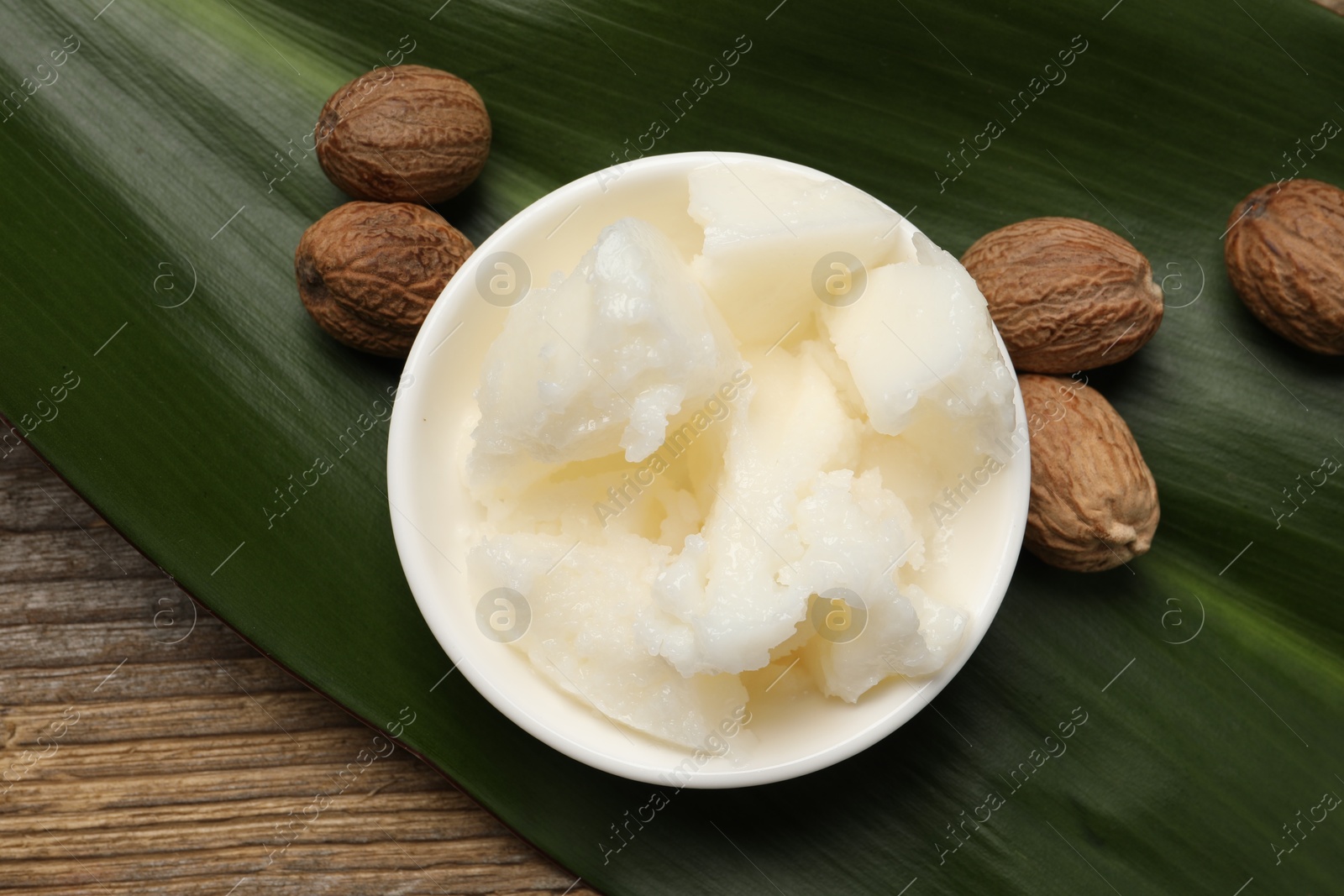 Photo of Natural shea butter in bowl, nuts and green leaf on wooden table, top view