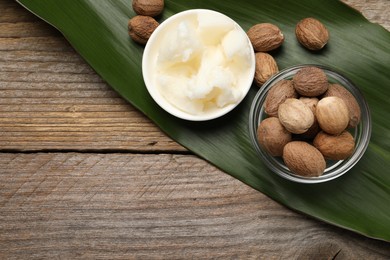 Natural shea butter in bowl, nuts and green leaf on wooden table, top view. Space for text