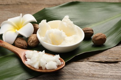 Natural shea butter in bowl, spoon, nuts, plumeria flower and green leaf on wooden table