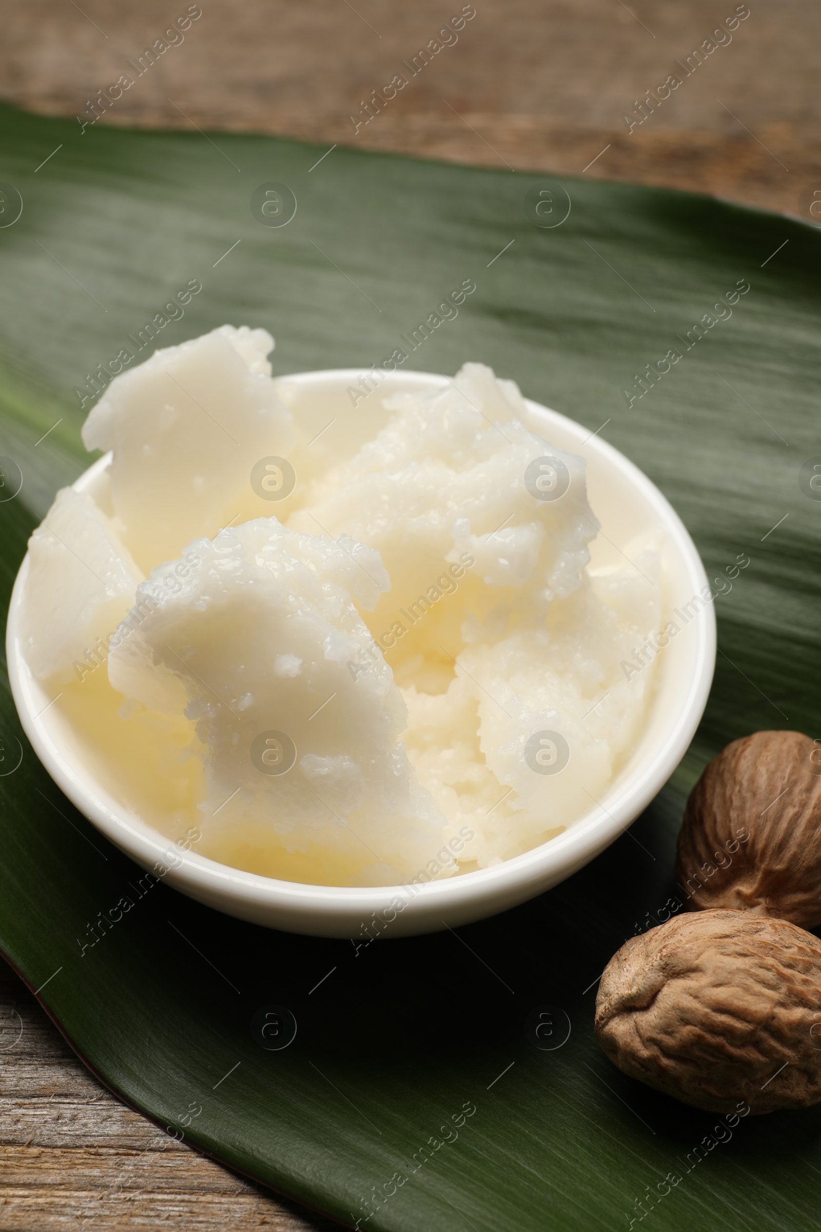 Photo of Natural shea butter in bowl, nuts and green leaf on wooden table