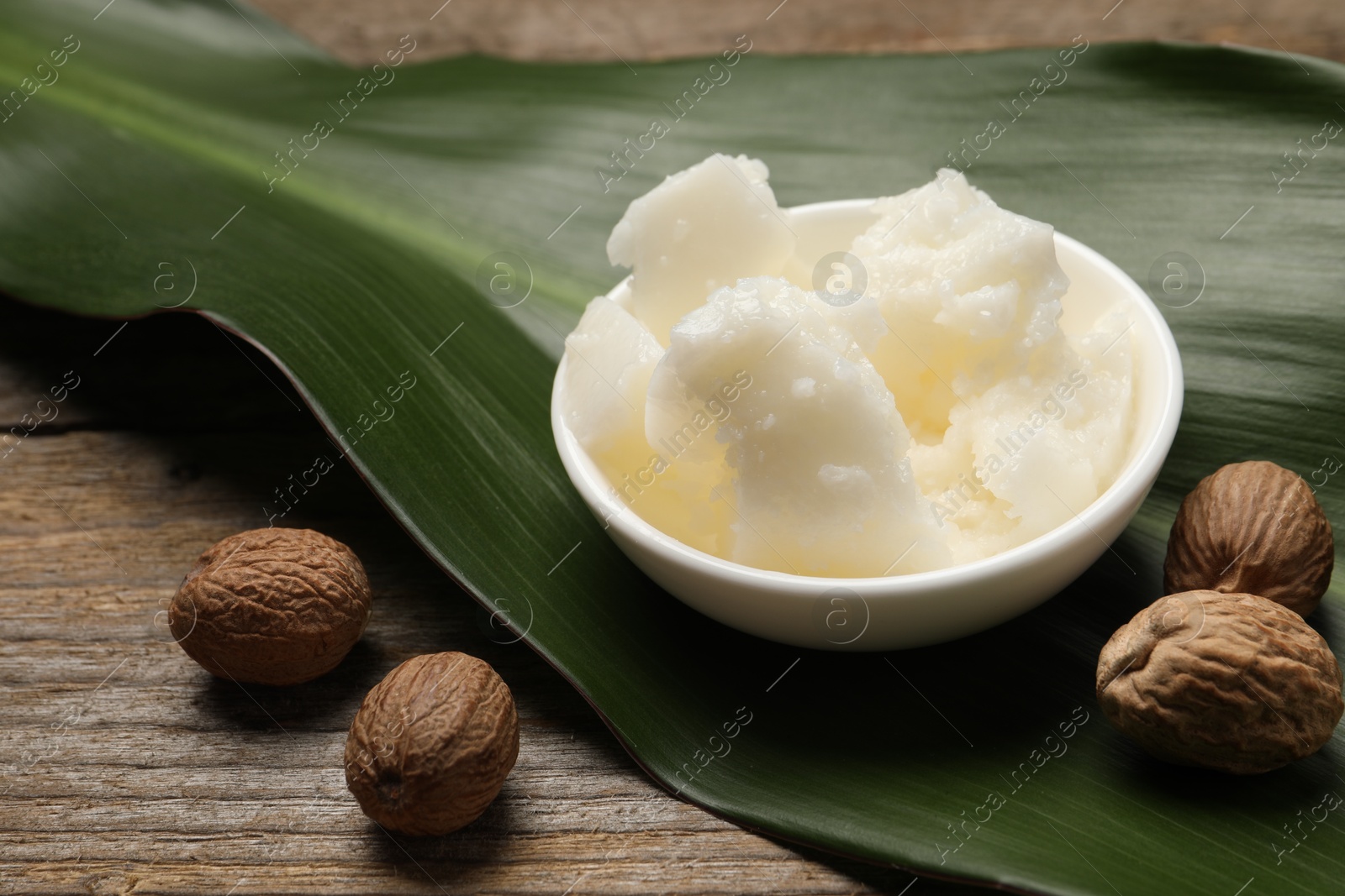 Photo of Natural shea butter in bowl, nuts and green leaf on wooden table