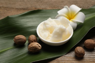 Natural shea butter in bowl, nuts, plumeria flower and green leaf on wooden table