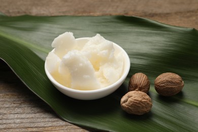 Photo of Natural shea butter in bowl, nuts and green leaf on wooden table