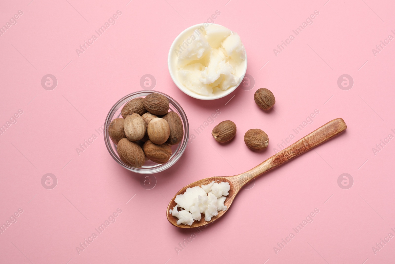 Photo of Natural shea butter in bowl, spoon and nuts on pink background, top view