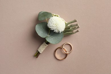 Small stylish boutonniere and rings on beige background, top view