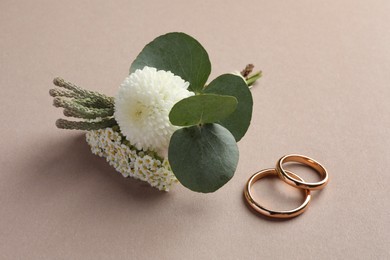 Small stylish boutonniere and rings on beige background