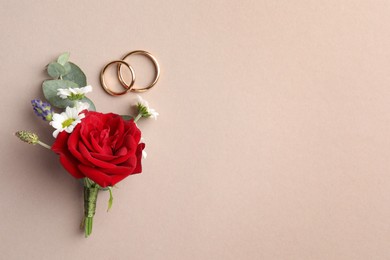 Small stylish boutonniere and rings on beige background, top view. Space for text