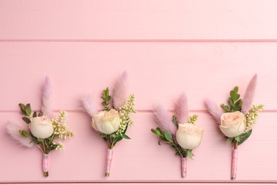 Many small stylish boutonnieres on pink wooden table, flat lay