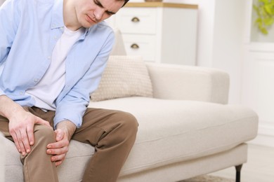 Photo of Man suffering from knee pain on sofa indoors, closeup