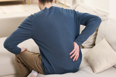 Photo of Man suffering from back pain on sofa indoors, closeup