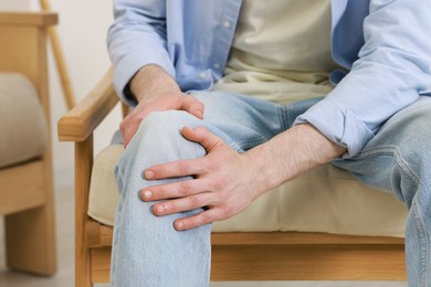 Man suffering from knee pain in armchair indoors, closeup