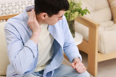 Man suffering from pain in his neck indoors