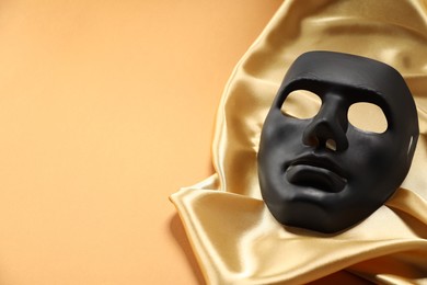 Theater arts. Black mask and golden fabric on pale orange background, space for text