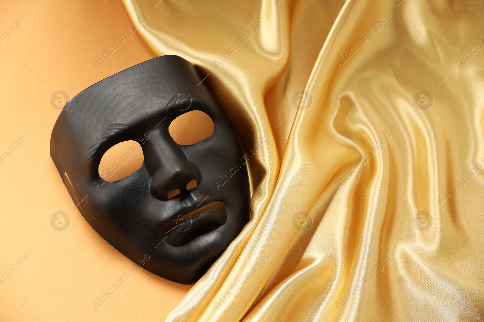 Photo of Theater arts. Black mask and golden fabric on pale orange background, closeup