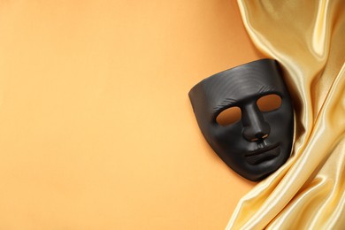 Photo of Theater arts. Black mask and golden fabric on pale orange background, top view. Space for text