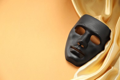 Photo of Theater arts. Black mask and golden fabric on pale orange background, top view. Space for text