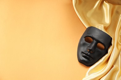 Theater arts. Black mask and golden fabric on pale orange background, top view. Space for text