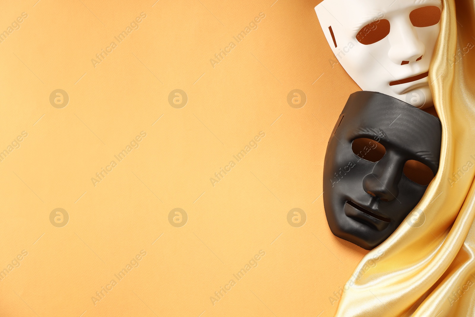 Photo of Theater arts. Two masks and golden fabric on pale orange background, top view. Space for text