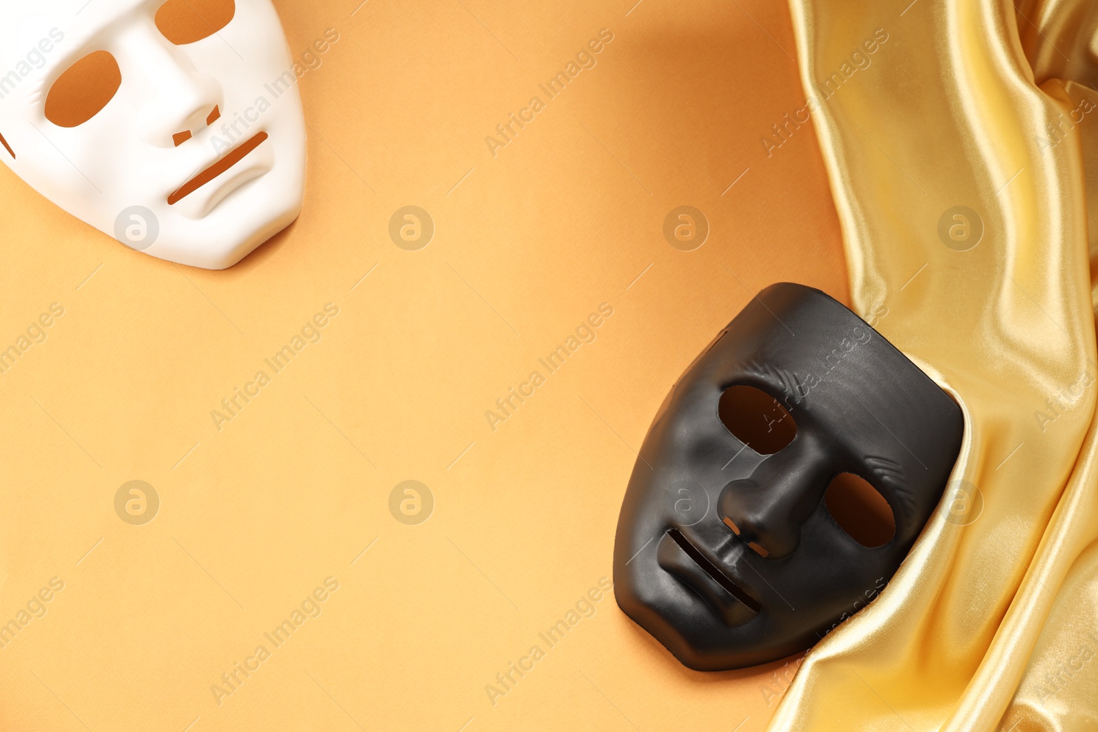 Photo of Theater arts. Two masks and golden fabric on pale orange background, top view. Space for text