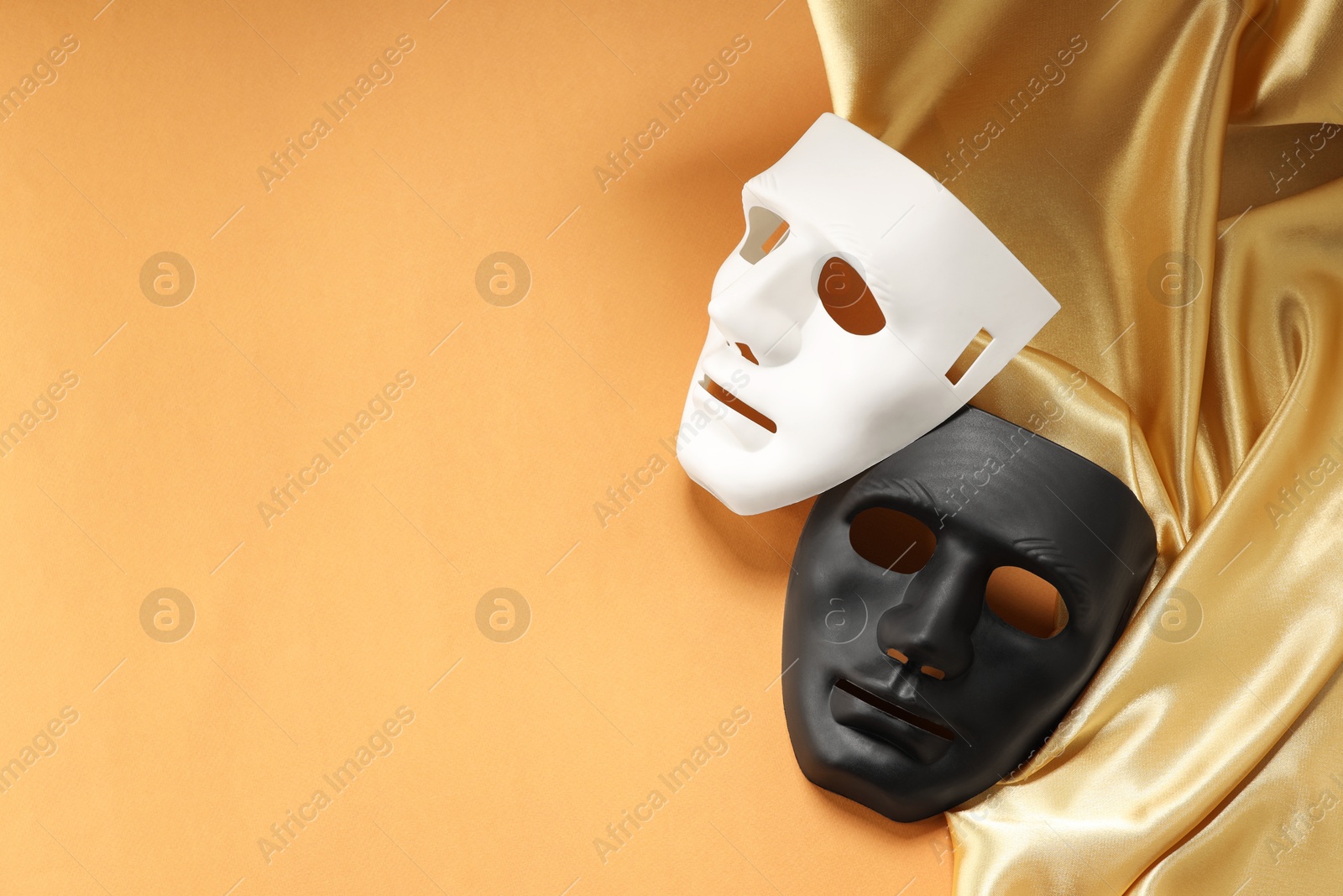 Photo of Theater arts. Two masks and golden fabric on pale orange background, above view. Space for text