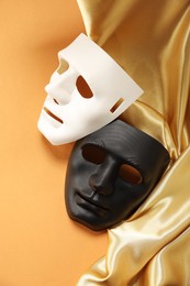 Photo of Theater arts. Two masks and golden fabric on pale orange background, above view