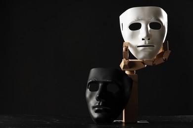 Photo of Wooden mannequin hand and plastic masks on black background, space for text. Theatrical performance