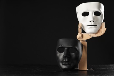 Photo of Wooden mannequin hand and plastic masks on black background, space for text. Theatrical performance