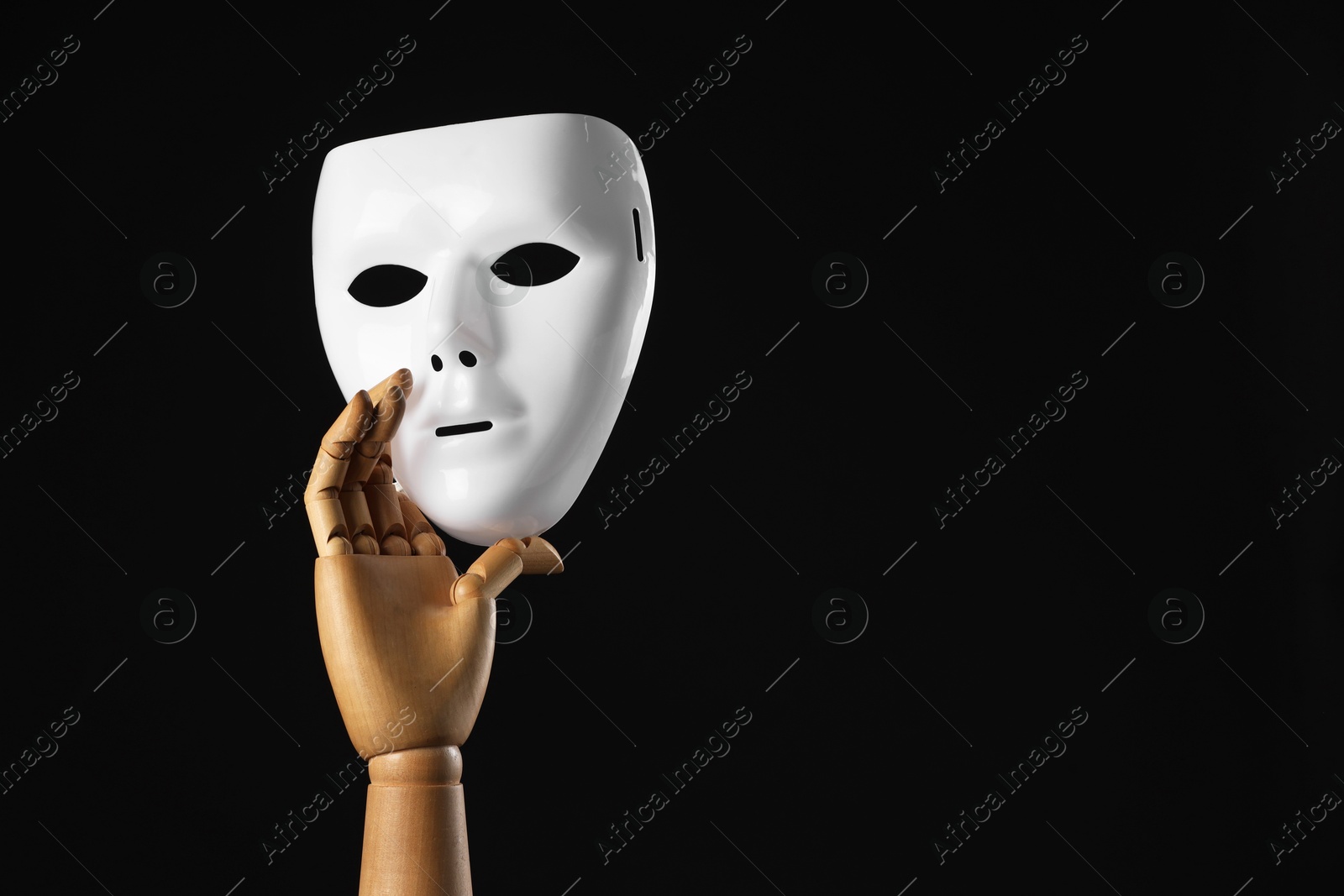 Photo of Wooden mannequin hand holding plastic mask on black background, space for text. Theatrical performance