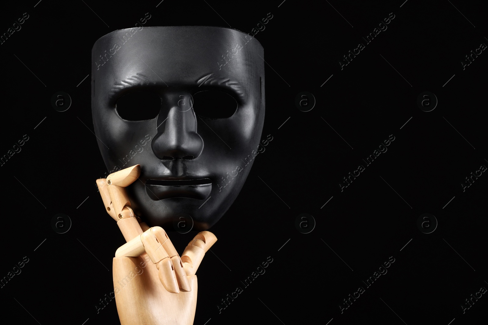 Photo of Wooden mannequin hand holding plastic mask on black background, space for text. Theatrical performance